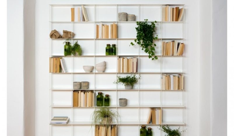 A modern, white, wall-mounted bookshelf filled with books, green plants, and decorative items.