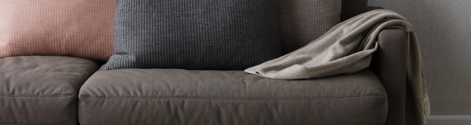 A close-up of a modern, plush sofa adorned with a mix of textured cushions in shades of peach, gray, and charcoal, complemented by a taupe throw blanket elegantly draped over one side.