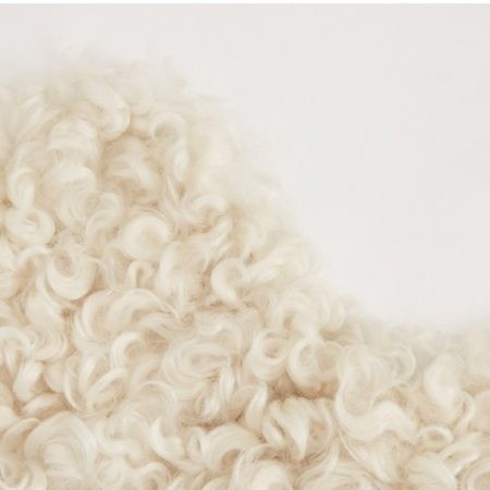 Close-up view of a Gotland sheepskin throw, showcasing its soft, curly, white wool texture. The image highlights the intricate details of the fleece, emphasizing its fluffiness and warmth.