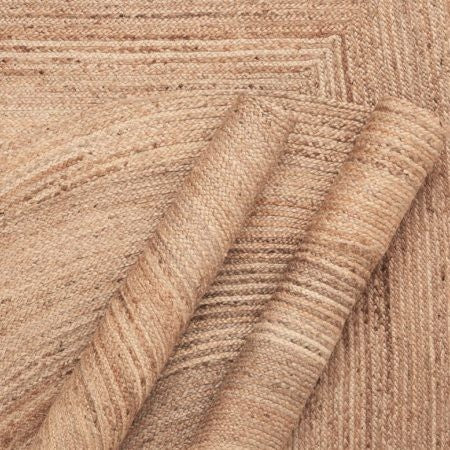 A detailed view of a natural jute braided rug, showing the intricate weave and rich texture. The rug's fibers are closely intertwined in a spiral pattern, demonstrating skilled craftsmanship.