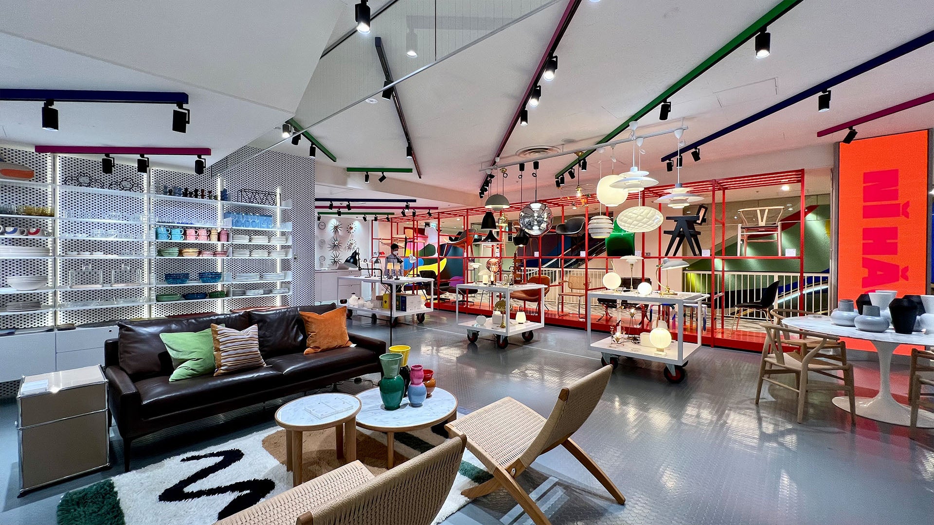 A vibrant and modern interior view of The Conran Shop in Kobe, with a colorful layout featuring a variety of home decor items. The store includes sections with different furniture like sofas, chairs, and tables, displayed among eclectic accessories such as lamps, vases, and textiles.