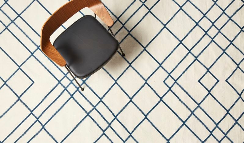 A black chair with wooden armrests is placed on a white rug with a blue geometric pattern.