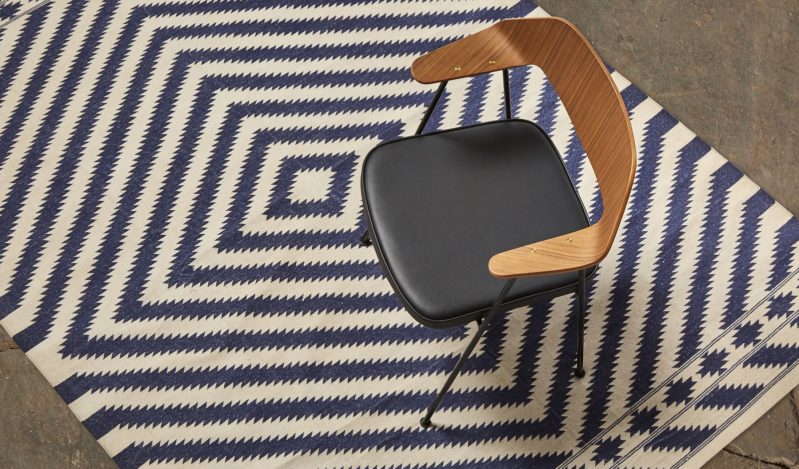 A black chair with wooden armrests is placed on a blue and white geometric patterned rug.