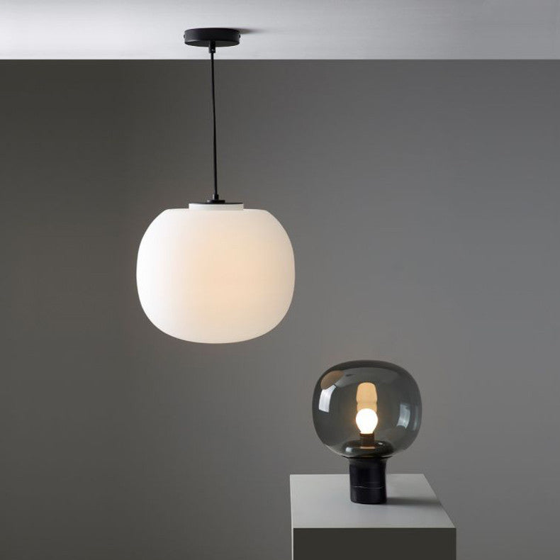 A modern lighting setup featuring a Flo ceiling pendant light with a white globe shade and a Flo table lamp with a smoky gray glass shade, displayed against a minimalist gray background.