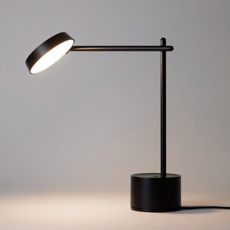 A sleek black Roto Table Lamp with a round base and an adjustable arm, casting light downward.
