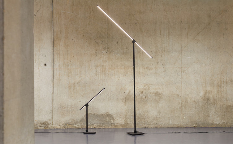 Two Axis Task Lamps against a concrete wall, one in a taller floor model and the other in a shorter desk model.