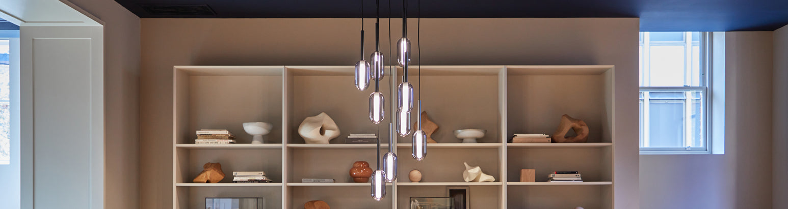 A room with a pendant light fixture hanging from the ceiling in front of a wall of shelves displaying various decorative items.